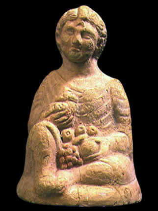 Statuetta che raffigura il dio Shaprada, presentato sotto i tratti di un bambino seduto che tiene in mano una manciata di frutti