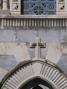 Particolare della croce che si trova all'apice dell'arco acuto della porta di accesso all'area cimiteriale