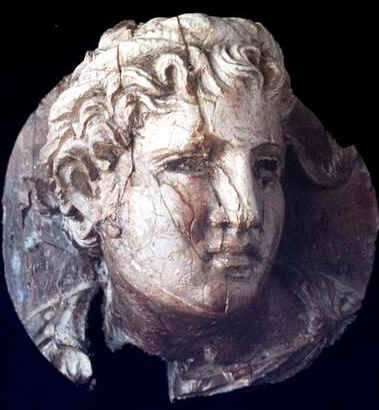 Applique rotonda tagliata con avorio e che raffigura la testa di un adolescente eseguito con estrema precisione ed eleganza. L'opera proviene da Cartagine ed è attribuita al IV-III sec. a. C. E' conservata al Museo del Bardo