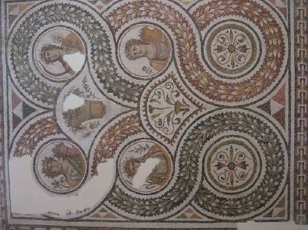 Mosaico con tondi e figure dalla casa delle colonne rosse. Il mosaico faceva partedi una sala absidale: ha una cornice a dentici con medaglioni circolari e due oculi. I due medaglioni a destra contengono fiori a forma di croce, gli altri presentano busti di donne e sono le 4 stagioni con i loro attributi floreali. Troviamo un paniere con uva (autunno), grano (estate), rami d'ulivo (inverno) e rose (primavera)